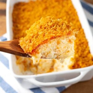 Funeral Potatoes on a wood spoon in front of baking dish