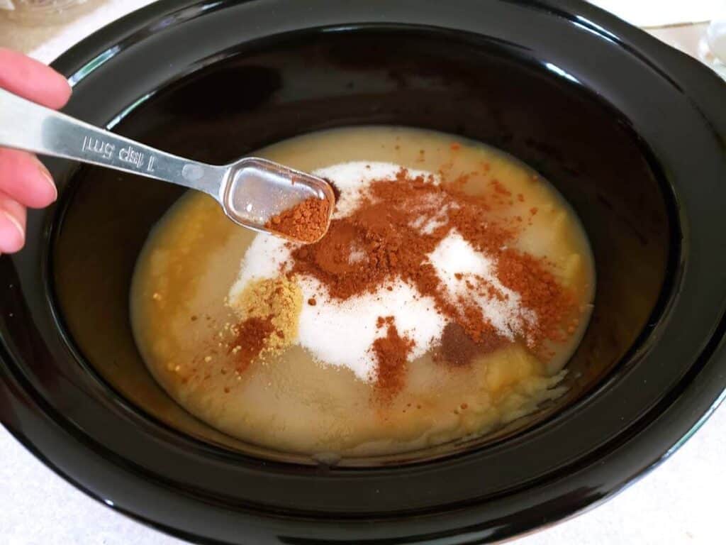 adding sugar and spices to the applesauce in the crock