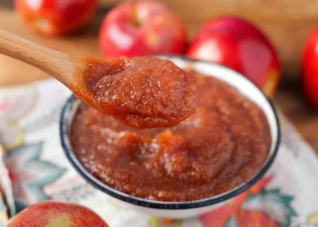 apple butter in a white bowl with a wood spoonful above