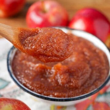 apple butter in a white bowl with a wood spoonful above