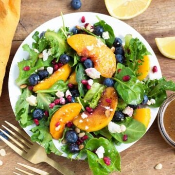 Peach Salad with Blueberries and Feta on a white plate, wood background, from above