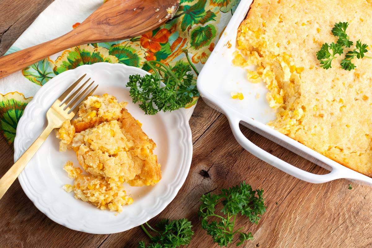 corn casserole on a white plate in front of casserole dish