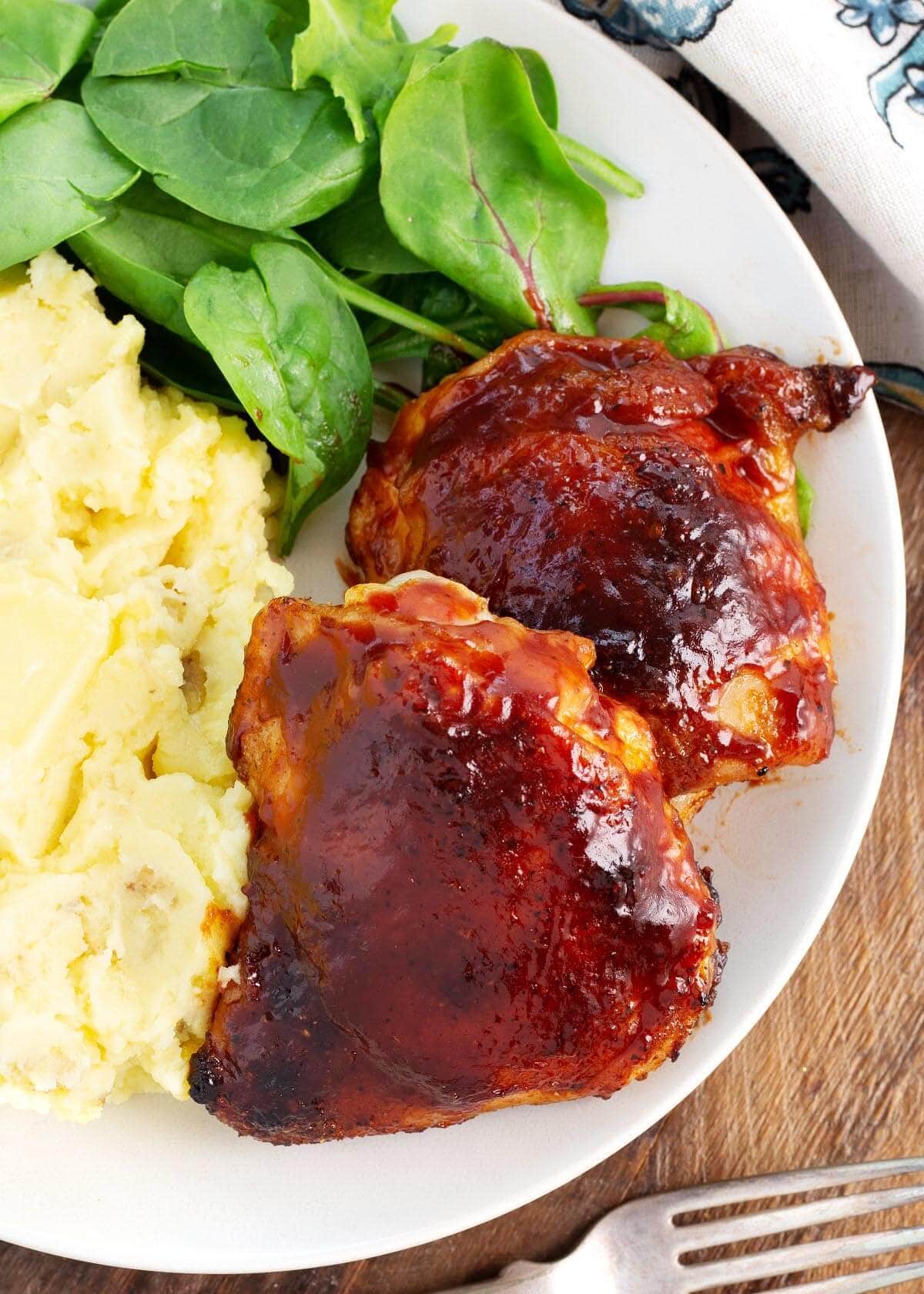 baked bbq chicken thighs on a white plate with side dishes