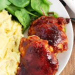 Oven Baked BBQ Chicken Thighs on a plate with salad and potatoes