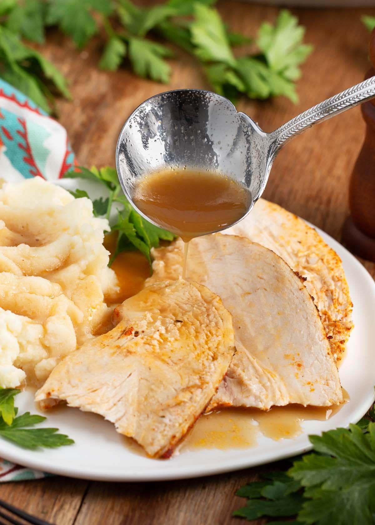 Chicken slices on a white plate with potatoes and ladle with gravy