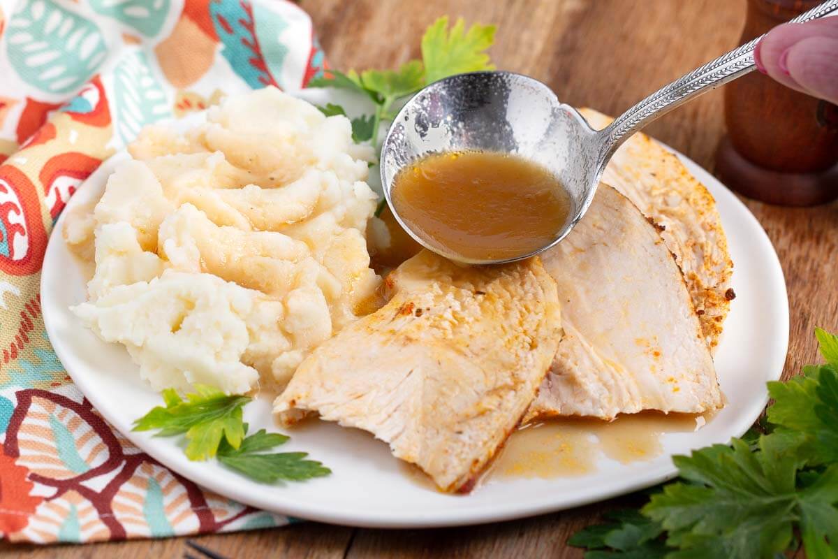 Chicken slices on a white plate with potstoes and ladle with gravy