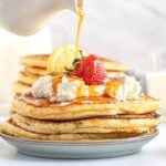 stack of Lemon Ricotta Pancakes with toppings and syrup pouring on them.