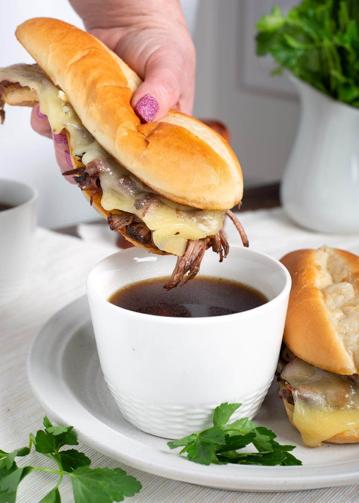 Slow Cooker French Dip Sandwich being dipped in jus