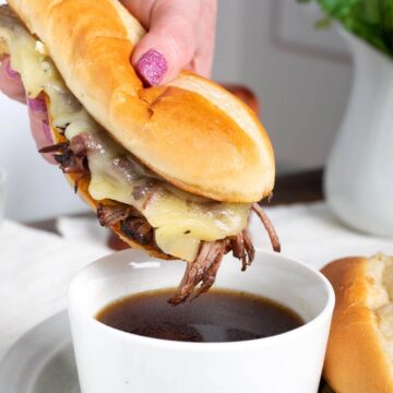 French Dip Sandwich held above a cup of jus.