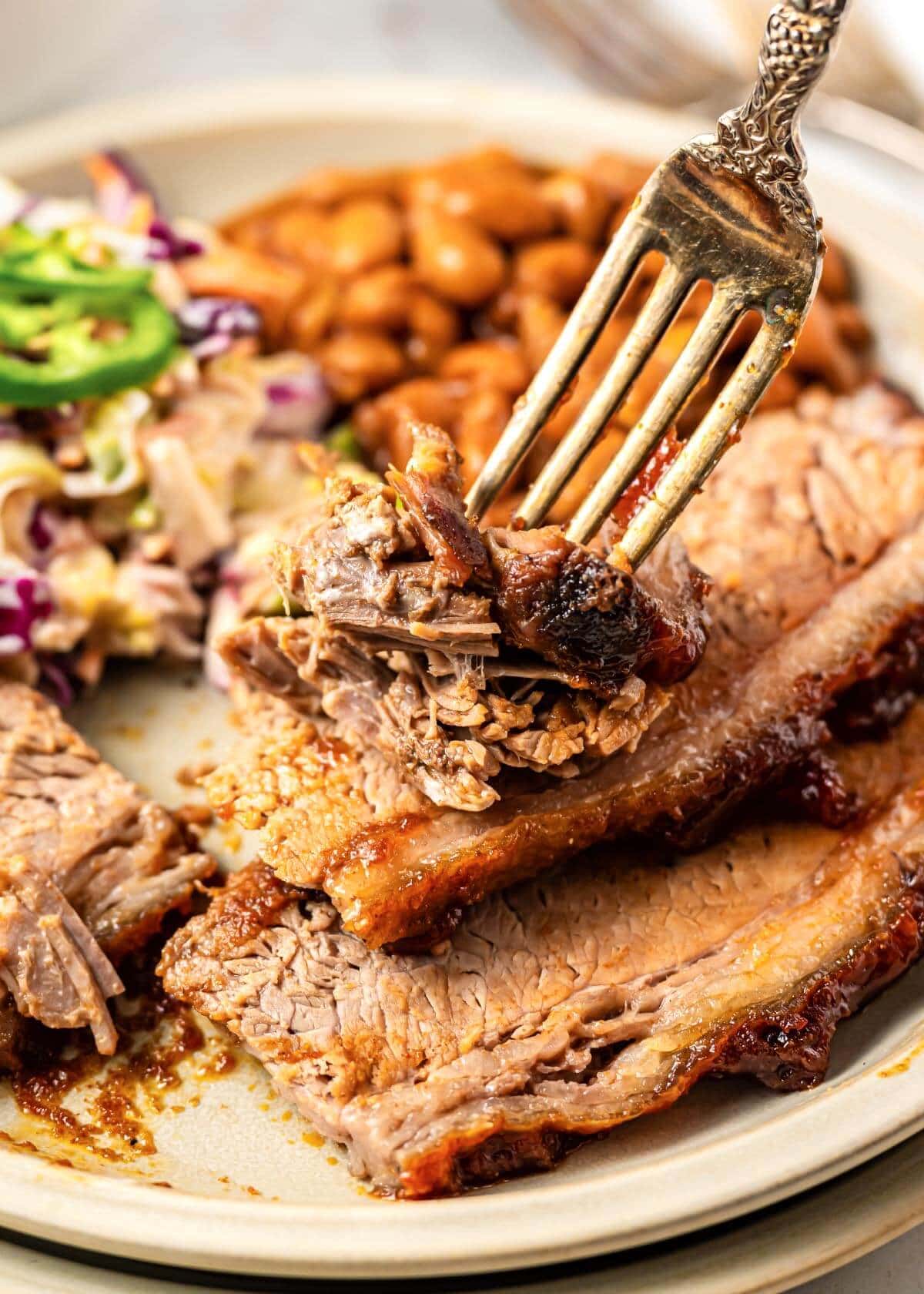 Brisket on a plate with beans and salad and fork.