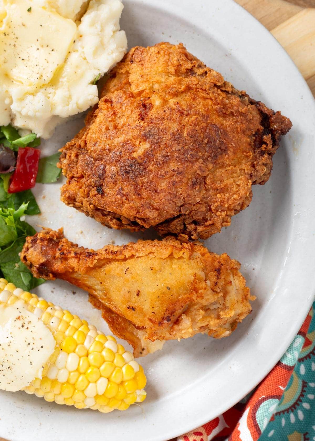 2 pieces of fried chicken on a plate with corn and potatoes