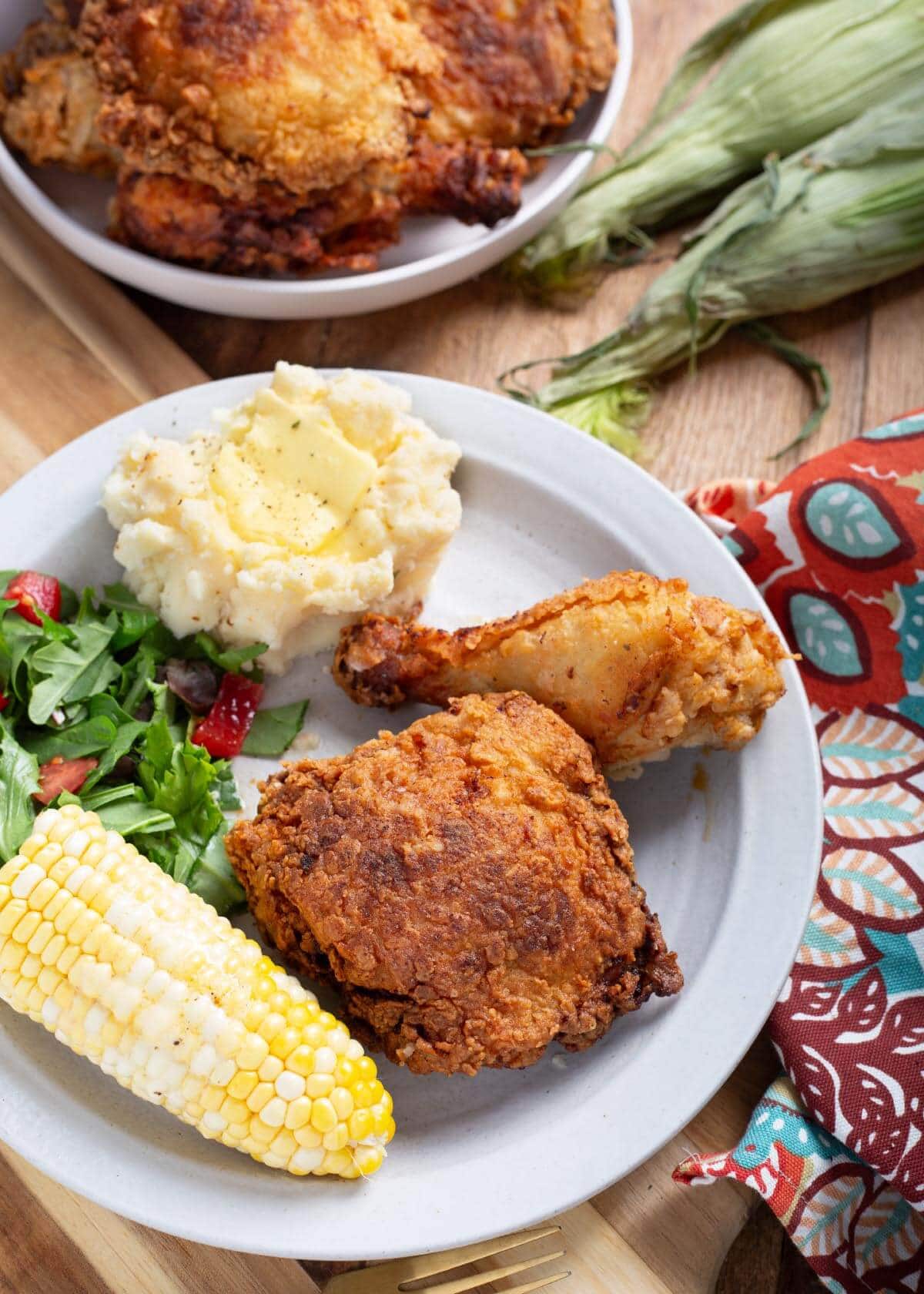 plate of 2 piece fried chicken with corn and potatoes.