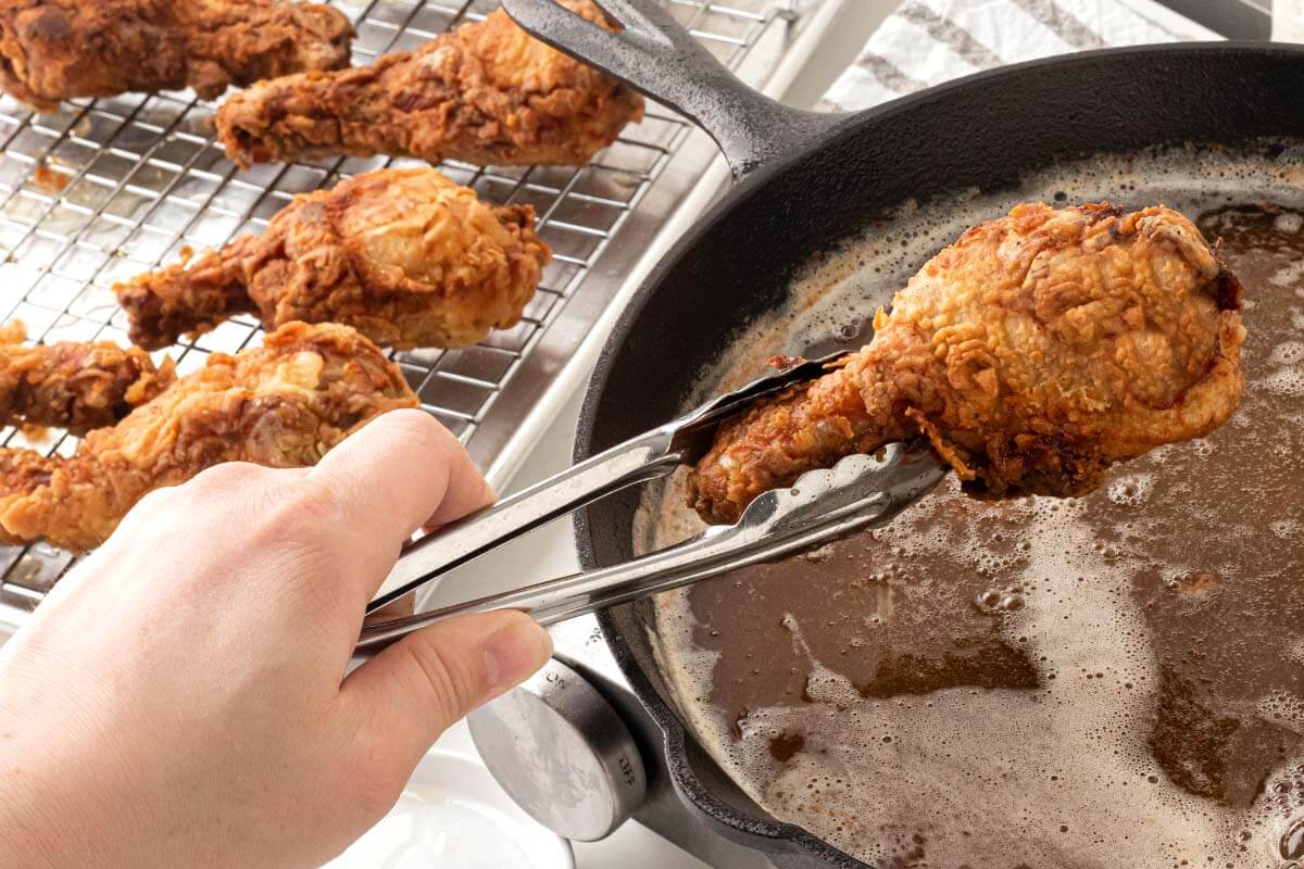 taking fried chicken from pan to wire rack.