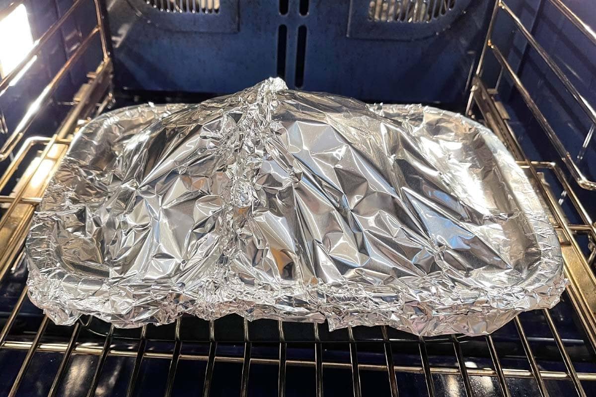Brown Sugar Glazed Spiral Ham in a baking dish in the oven covered with foil.