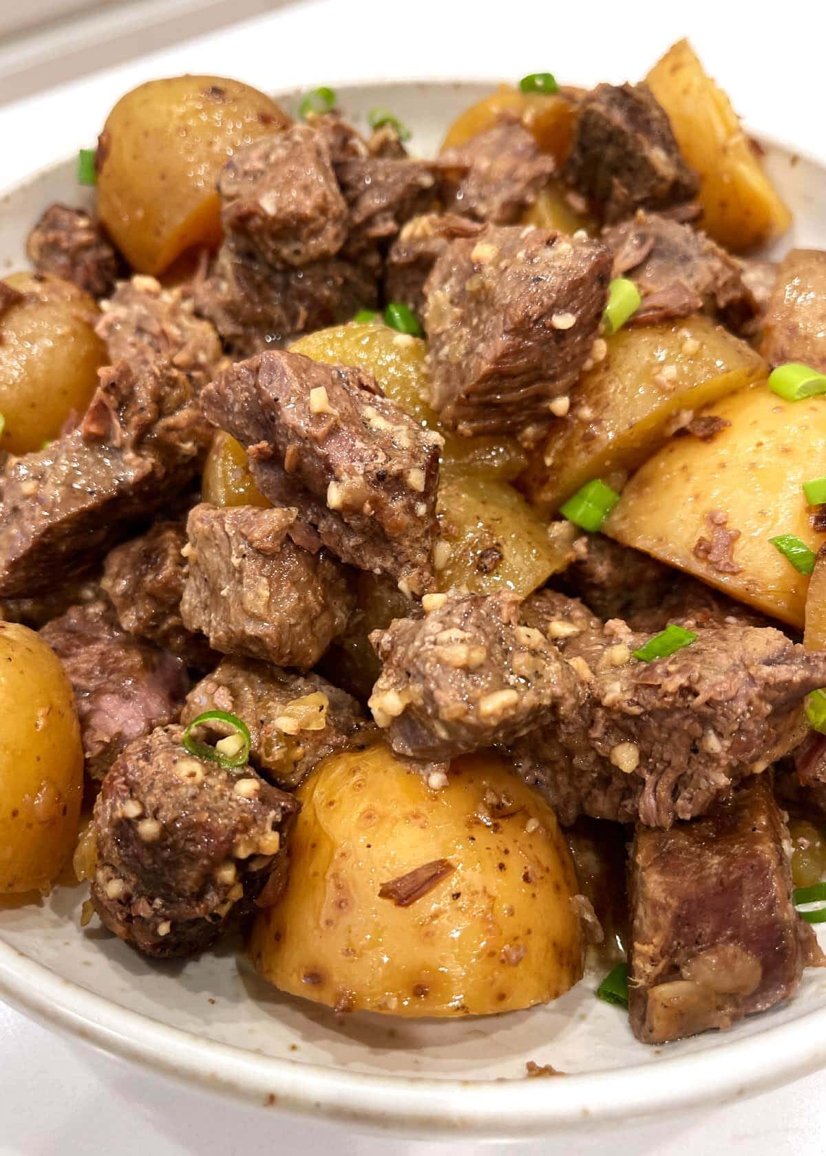Slow Cooker Garlic Butter Steak Bites and Potatoes in a white dish