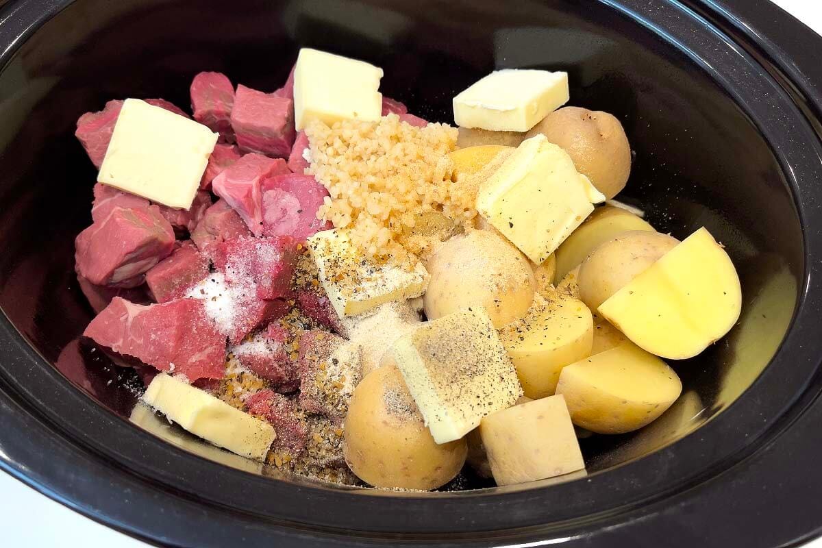 Slow Cooker Garlic Butter Steak Bites and Potatoes in a black crock