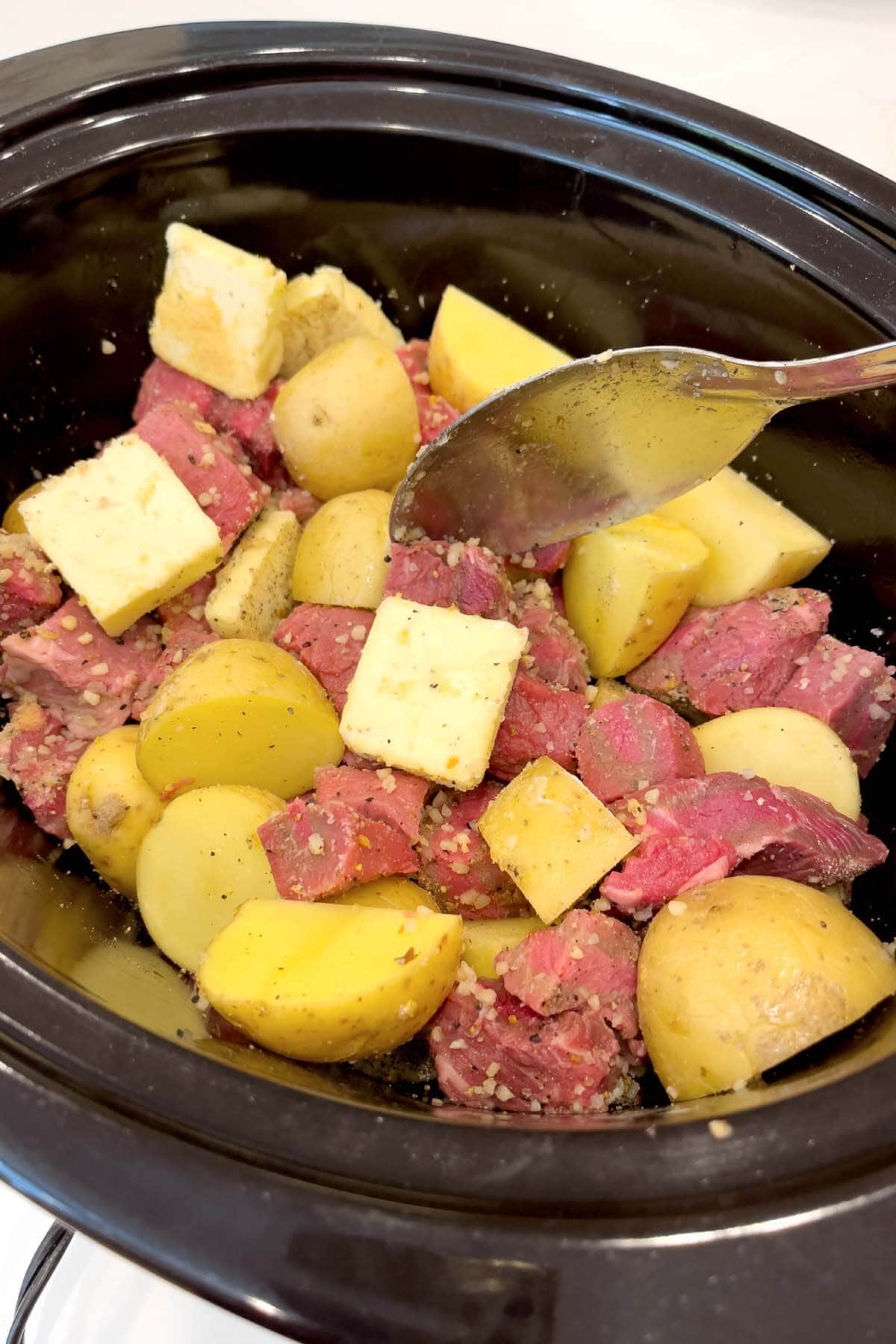 Slow Cooker Garlic Butter Steak Bites and Potatoes in a black crock